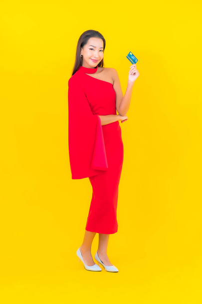 Muotokuva kaunis nuori aasialainen nainen luottokortilla keltaisella taustalla - Valokuva, kuva
