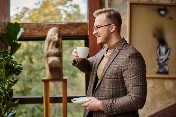 wesoły wyrafinowany lider biznesu z okularami w eleganckim garniturze pijący swoją gorącą kawę - Zdjęcie, obraz