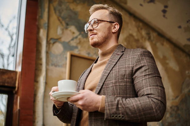 vidám, kifinomult üzleti vezető, elegáns öltönyös szemüveggel, forró kávéját issza. - Fotó, kép