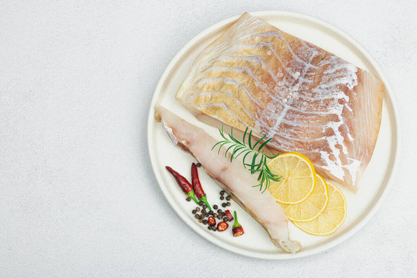 Raw pollock (Pollachius virens) fillet. Fresh fish for healthy food lifestyle. Lemon, rosemary, sea salt, chili, black peppercorn. Light stone concrete background, flat lay, top view - Photo, Image
