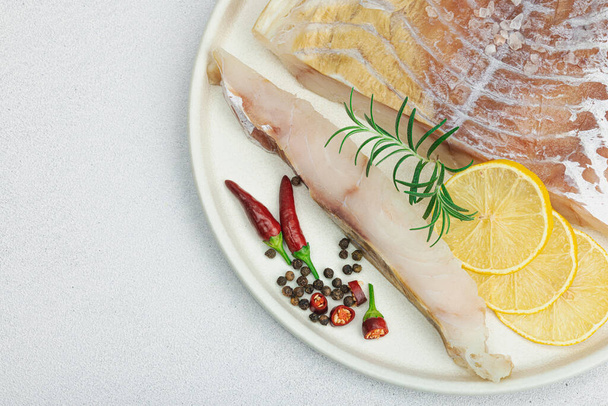 Raw pollock (Pollachius virens) fillet. Fresh fish for healthy food lifestyle. Lemon, rosemary, sea salt, chili, black peppercorn. Light stone concrete background, flat lay, top view - Photo, Image