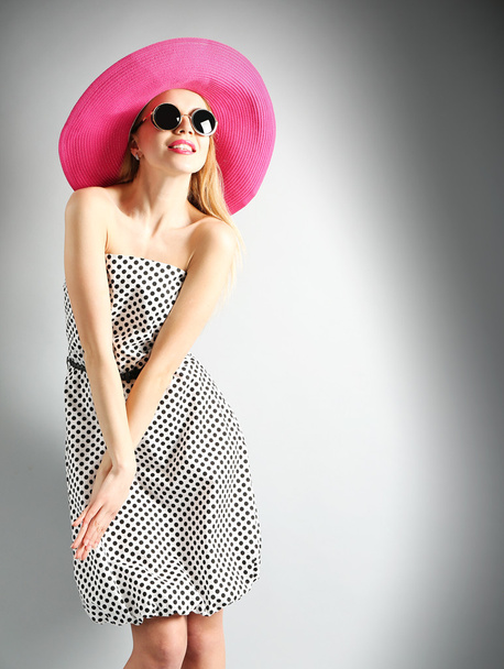 Expressive young model in pink hat with sunglasses on gray background - Фото, зображення