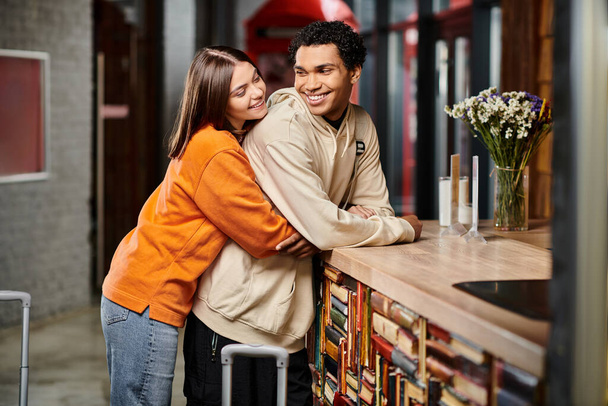 A romantic moment shared between a man and woman, as they embrace at reception desk in hostel - Photo, Image