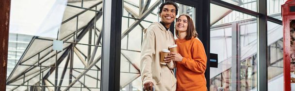 Fiatal változatos pár mosolyog, miközben kávét tart, hogy menjen, és belépjen egy modern hostel, banner - Fotó, kép