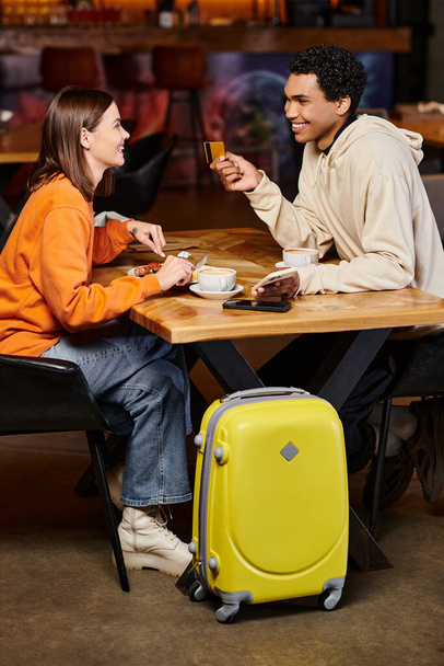 pareja diversa almorzando y haciendo compras en línea cerca de su equipaje en la cafetería albergue, tarjeta de crédito - Foto, Imagen