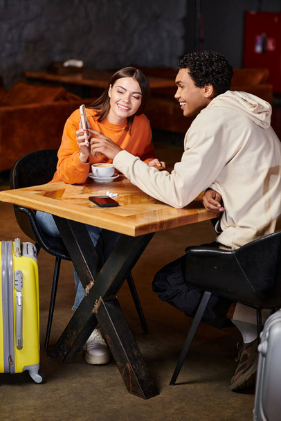 black man and happy woman using smartphone while sitting at table with coffee in cafe - Fotografie, Obrázek