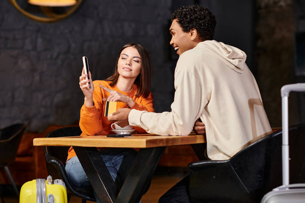 black man holding credit card while his girlfriend using smartphone near coffee cups in cafe - Photo, Image
