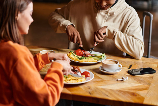 ποικίλο ζευγάρι απολαμβάνοντας πρωινό με νόστιμη ομελέτα, και λουκάνικα κοντά σε φλιτζάνια καφέ - Φωτογραφία, εικόνα