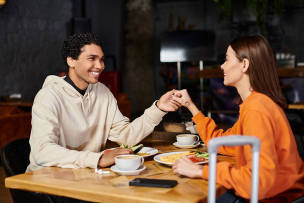 cheerful diverse couple enjoying a delicious meal in the charming indoor restaurant, holding hands - Photo, Image