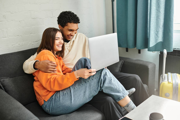 diverse couple snuggle on couch with their faces illuminated by the glow of the laptop screen, movie - Photo, Image