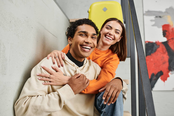 alegre pareja interracial en traje casual contra un telón de fondo de una pared de ladrillo en el albergue - Foto, imagen