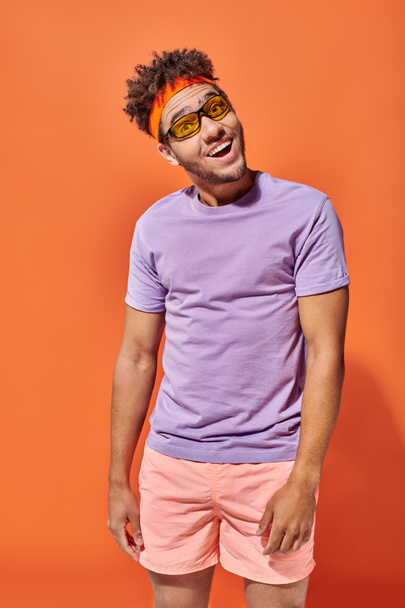 ワクワクする若いアフリカ系アメリカ人男性の眼鏡とオレンジ色の背景にカジュアルな服装, フェラ - 写真・画像