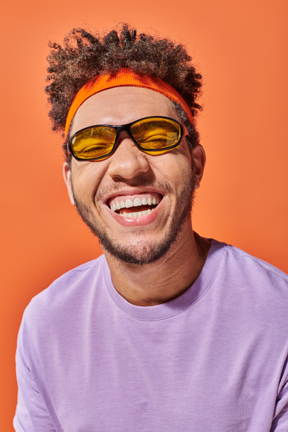 happy african american man in eyeglasses smiling with closed eyes on orange background, optimistic - Photo, Image
