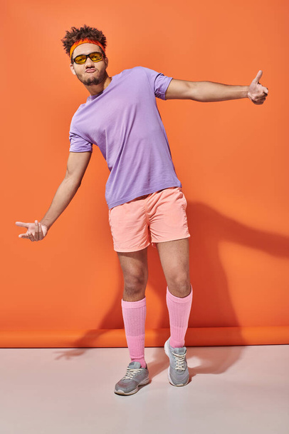 cool african american sportsman in gym attire and sunglasses gesturing on orange background - Photo, Image