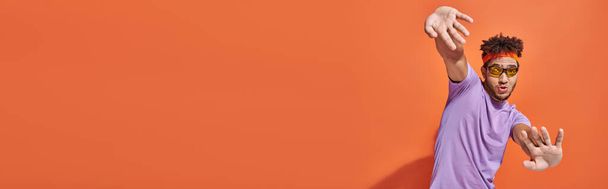 funny african american man in eyeglasses and headband looking at camera on orange background, banner - Foto, Imagem
