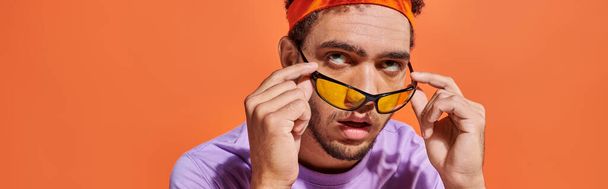 otrávený africký Američan v brýlích a čelence zvlněné oči na oranžovém pozadí, prapor - Fotografie, Obrázek