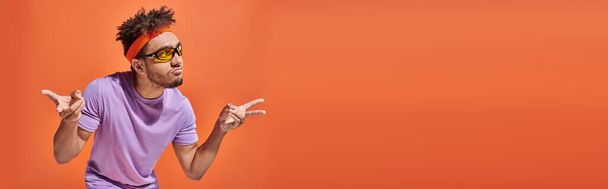 Αφροαμερικάνος με γυαλιά ηλίου που μουτρώνει τα χείλη και κάνει χειρονομίες σε πορτοκαλί φόντο, λάβαρο - Φωτογραφία, εικόνα