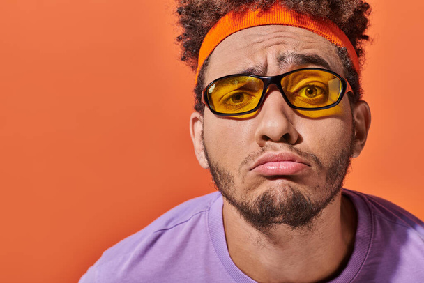 aufgebracht afrikanisch-amerikanischer Mann mit Brille und Stirnband grinst auf orangefarbenem Hintergrund, Fratze - Foto, Bild