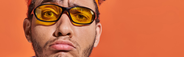 upset african american man in eyeglasses and headband grinning on orange background, grimace banner - Photo, Image