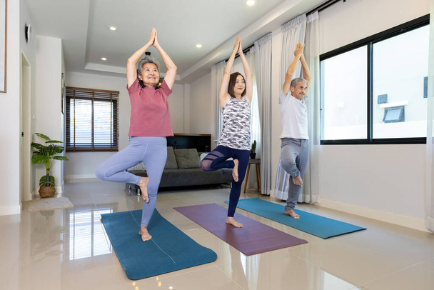 Starsza para azjatycka i córka robią trening w domu w stojącej pozycji równoważącej jogę dla relaksujących ćwiczeń i starszych zdrowych - Zdjęcie, obraz