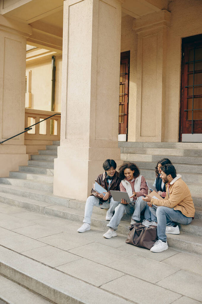 Χαμογελώντας φοιτητές με φορητό υπολογιστή είναι σπουδές σε εξωτερικούς χώρους κάθεται κοντά στο πανεπιστήμιο. Εκπαιδευτική έννοια - Φωτογραφία, εικόνα