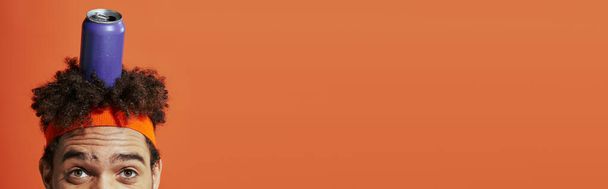 μωβ κουτάκι σόδας στο κεφάλι του κατσαρομάλλη Αφροαμερικανού με κορδέλα στο πορτοκαλί φόντο, λάβαρο - Φωτογραφία, εικόνα