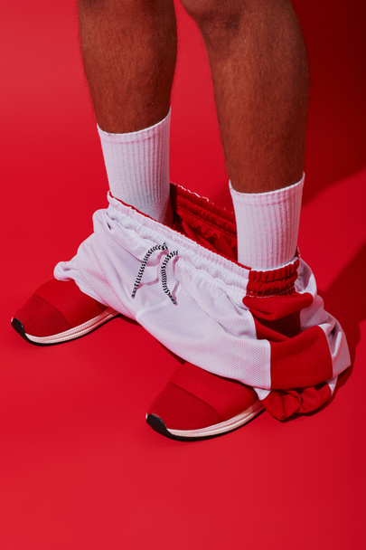 konceptuális fotó, kivágott férfi tornacipőben, fehér zokni és kocogók álló piros háttér - Fotó, kép