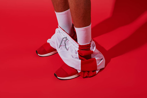 foto conceitual, homem cortado em tênis, meias brancas e corredores de pé no fundo vermelho - Foto, Imagem