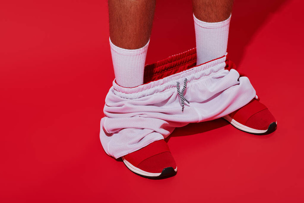 Modefotografie, beschnittener Mann in Turnschuhen, weißen Socken und Joggern auf rotem Hintergrund - Foto, Bild