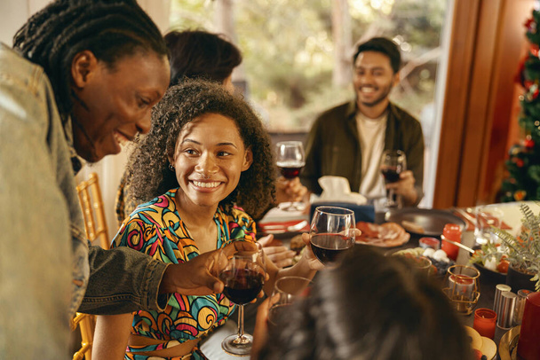 Группа улыбающихся друзей, наслаждающихся общением и выпивающих вино во время рождественской вечеринки дома - Фото, изображение