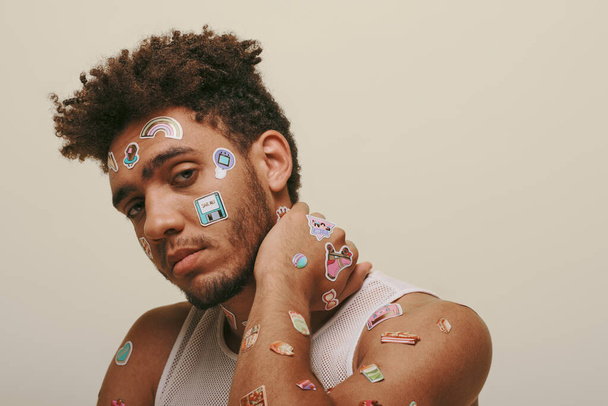 african american guy in tank top with stickers on face looking at camera on grey background - Photo, Image