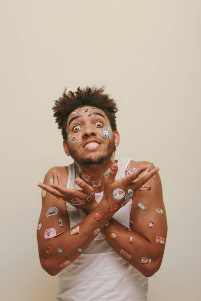 Эмоциональный африканский американец с наклейками на лице, жестикулирующий на сером фоне, хипстер - Фото, изображение