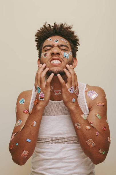 emotioneel Afro-Amerikaanse man met stickers op gezicht krabben baard op grijze achtergrond, hipster - Foto, afbeelding