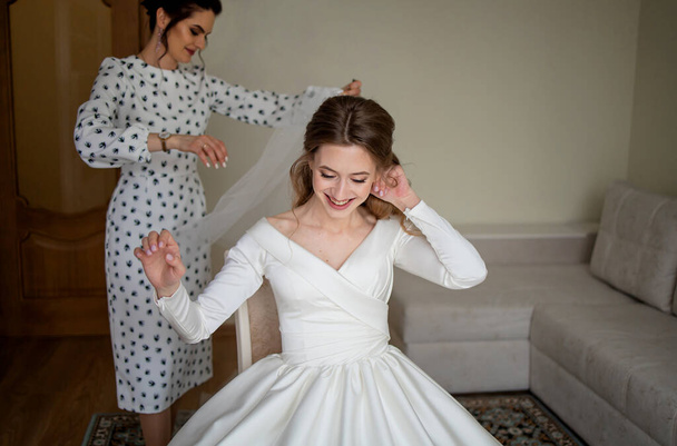 Una hermosa novia rubia en un vestido de lujo blanco se está preparando para la boda. Preparación matinal. Una mujer se pone un vestido. - Foto, Imagen
