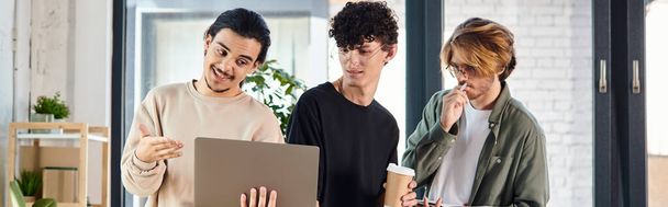 Drie jonge mannen betrokken bij een levendige discussie over een laptop in een coworking ruimte, opstarten banner - Foto, afbeelding