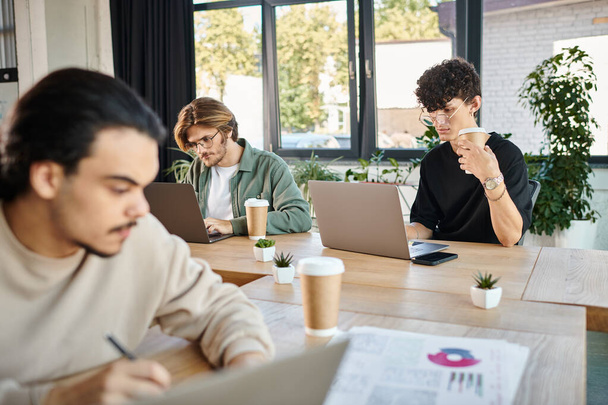 Jovens profissionais profundamente focados enquanto trabalham em laptops em um espaço de coworking, foreground borrado - Foto, Imagem
