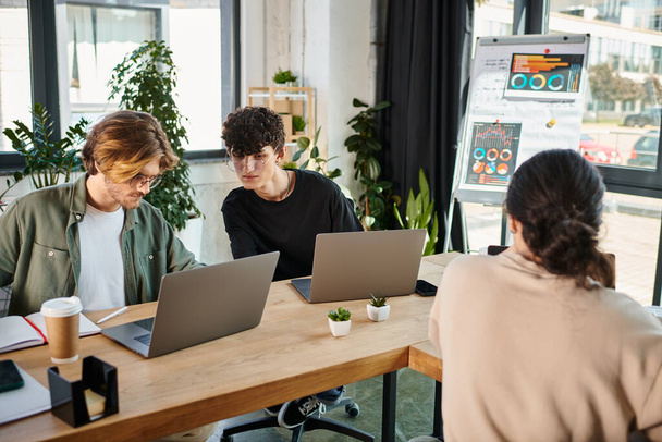 Jeunes professionnels dans la vingtaine partageant des idées près d'ordinateurs portables dans un espace de coworking, au premier plan flou - Photo, image