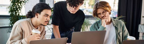 Młodzi mężczyźni po dwudziestce analizujący wspólnie projekt na laptopach w słonecznej przestrzeni dla współpracowników, start-up banner - Zdjęcie, obraz