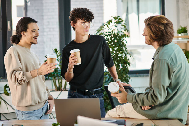 conversa amigável entre três jovens colegas de trabalho segurando café para ir no escritório moderno, inicialização - Foto, Imagem
