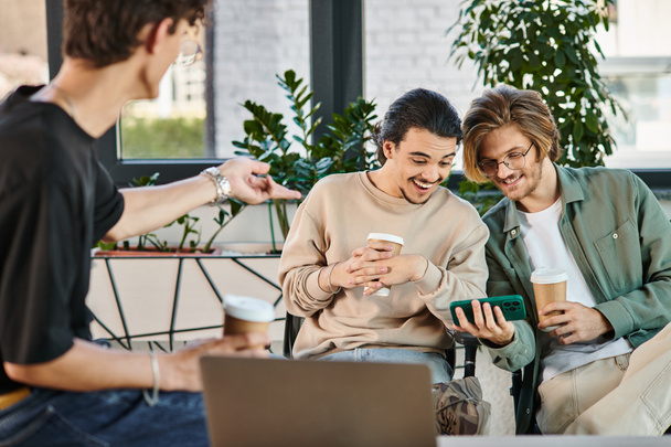 χαρούμενους νέους άνδρες κουβεντιάζοντας κατά τη διάρκεια του διαλείμματος καφέ στο γραφείο και βλέποντας βίντεο στο smartphone - Φωτογραφία, εικόνα