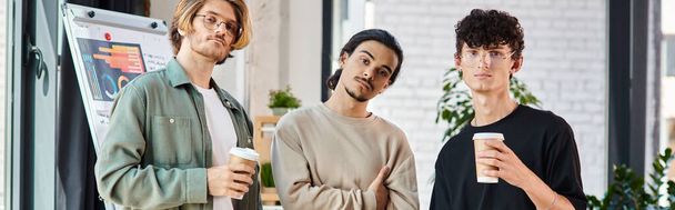 ambitni młodzi mężczyźni patrzący na baner z kamerą, trzej początkujący członkowie zespołu z kawą na wynos - Zdjęcie, obraz