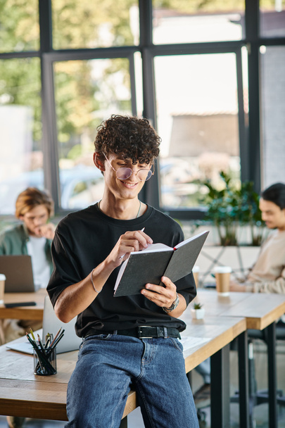 Curly-haired man with glasses smiling and taking notes in a dynamic office space, startup ideas - Photo, Image