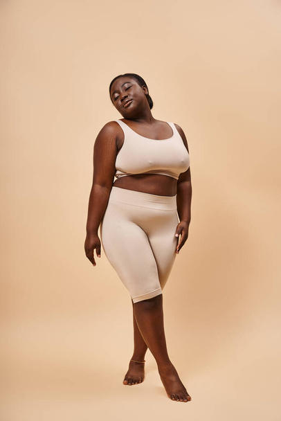 Graceful plus size african american model in beige attire posing against a matching backdrop - Photo, Image