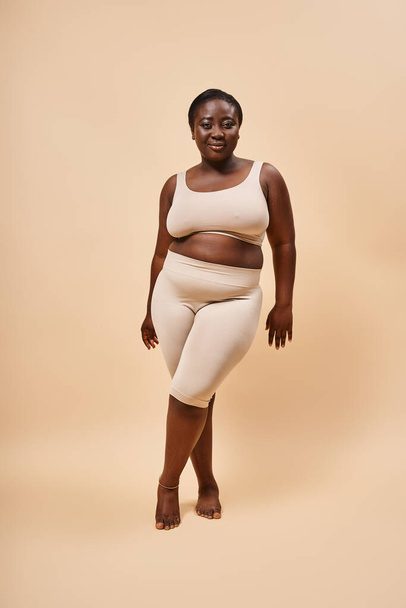плюс розмір афроамериканської моделі в бежевому вбранні позує на відповідний фон, позитивне тіло - Фото, зображення