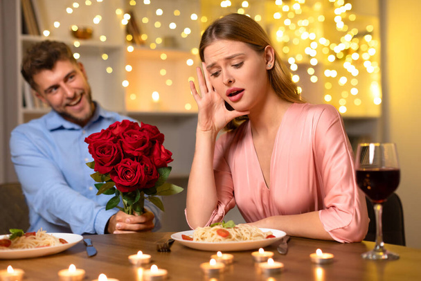 Mujer joven asombrada reacciona a ramo sorpresa de rosas del hombre sonriente, creando un momento dramático durante una cena romántica a la luz de las velas - Foto, Imagen