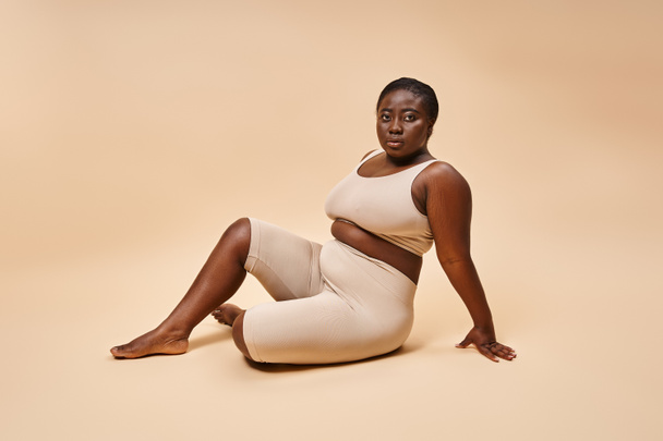 plus velikost africký americký mladý žena v béžové spodní prádlo pózovat proti odpovídající pozadí - Fotografie, Obrázek