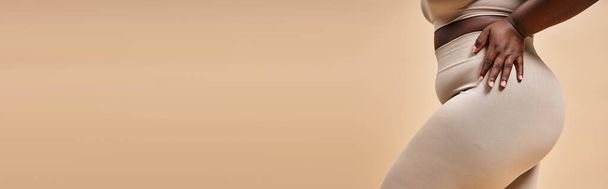 vista recortada de mujer afroamericana de talla grande en ropa interior posando sobre fondo beige, pancarta - Foto, imagen