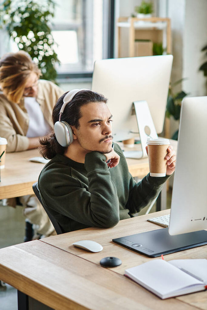 zamyšlený mužský profesionál ve sluchátkách drží kávu jít a při pohledu na monitor v kanceláři - Fotografie, Obrázek