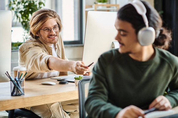 cheerful male professional in glasses passing his stylus pen to blurred coworker in headphones - Photo, Image