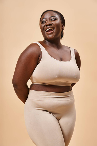 felice plus size donna in biancheria intima beige ridere in studio, corpo positivo e autostima - Foto, immagini